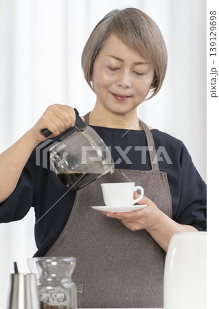 リビングでコーヒー豆を挽いてコーヒーを飲むシニア女性 リビングでコーヒー豆を挽いてコーヒーを飲むシニア女性 139129698