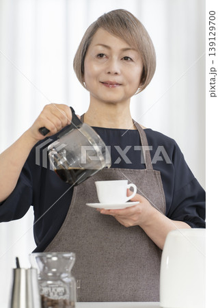 リビングでコーヒー豆を挽いてコーヒーを飲むシニア女性 リビングでコーヒー豆を挽いてコーヒーを飲むシニア女性 139129700