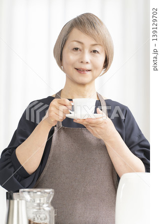 リビングでコーヒー豆を挽いてコーヒーを飲むシニア女性 リビングでコーヒー豆を挽いてコーヒーを飲むシニア女性 139129702