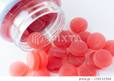 A close-up of vibrant red gummies placed next to a white container, highlighting their glossy texture and inviting appearance. A close-up of vibrant red gummies placed next to a white container, highlighting their glossy texture and inviting appearance. 139132568