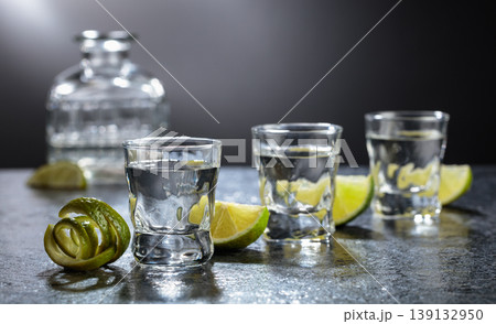 Vodka with lime slices on a black stone table. Vodka with lime slices on a black stone table. 139132950