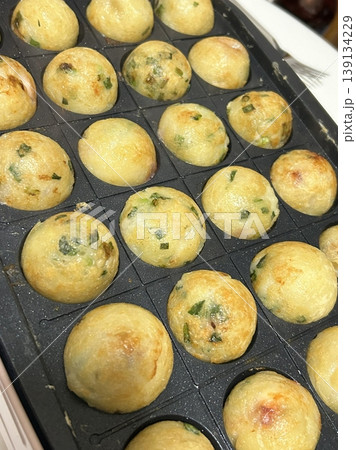 Takoyaki, a popular Japanese street food, are crispy round dough balls filled with octopus, tempura bits, and pickled ginger, topped with takoyaki sauce, bonito flakes, and aonori. 139134229