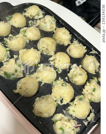 Takoyaki, a popular Japanese street food, are crispy round dough balls filled with octopus, tempura bits, and pickled ginger, topped with takoyaki sauce, bonito flakes, and aonori. 139134336