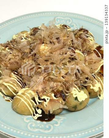 Takoyaki, a popular Japanese street food, are crispy round dough balls filled with octopus, tempura bits, and pickled ginger, topped with takoyaki sauce, bonito flakes, and aonori. Takoyaki, a popular Japanese street food, are crispy round dough balls filled with octopus, tempura bits, and pickled ginger, topped with takoyaki sauce, bonito flakes, and aonori. 139134337