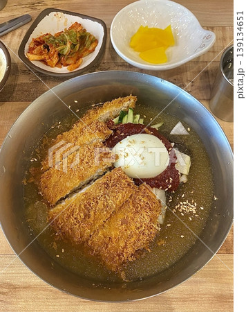 Cold naengmyeon noodles served in a chilled broth with sliced vegetables and egg, paired with crispy golden donkatsu, creating a balance of refreshing and savory flavors in one meal 139134651
