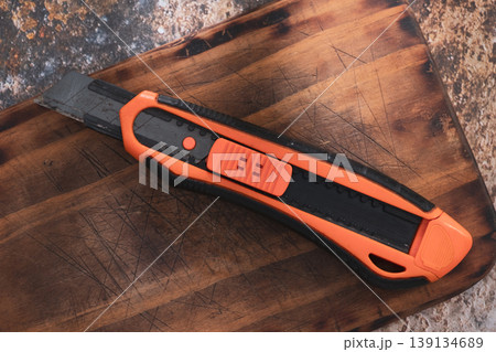 Orange Utility Cutter Knife on Wooden Cutting Board Orange Utility Cutter Knife on Wooden Cutting Board 139134689