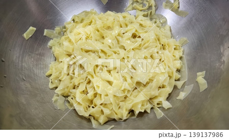 Freshly Cooked Wide Flat Egg Noodles in a Stainless Steel Mixing Bowl 139137986