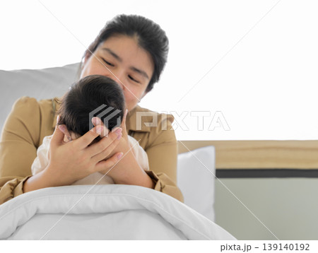 Mother holding head of her newborn baby girl or boy in hands. Loving mum sitting in white bed and holding infant child. 139140192
