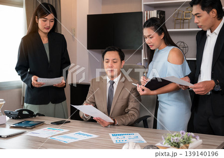 Professional team collaborates around office desk while reviewing documents and discussing business strategy Professional team collaborates around office desk while reviewing documents and discussing business strategy 139140196