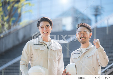 ヘルメットを持つ若手作業員のポートレート 建設現場と成長、ビル背景に未来や希望のカメラ目線ガッツポー ヘルメットを持つ若手作業員のポートレート 建設現場と成長、ビル背景に未来や希望のカメラ目線ガッツポー 139140307