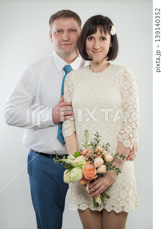 A woman holds a bouquet while hugging a man from behind in a studio. Both smile and look happy. A woman holds a bouquet while hugging a man from behind in a studio. Both smile and look happy. 139140352