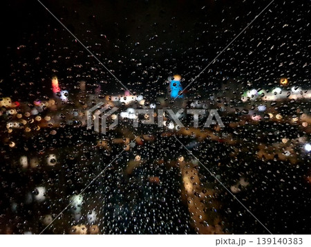 Raindrops on a window with city lights in the background at night Raindrops on a window with city lights in the background at night 139140383