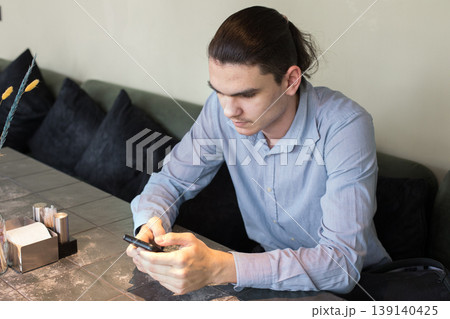 A man is seated at a table in a cafe. He holds a cup and appears to be lost in thought. A man is seated at a table in a cafe. He holds a cup and appears to be lost in thought. 139140425