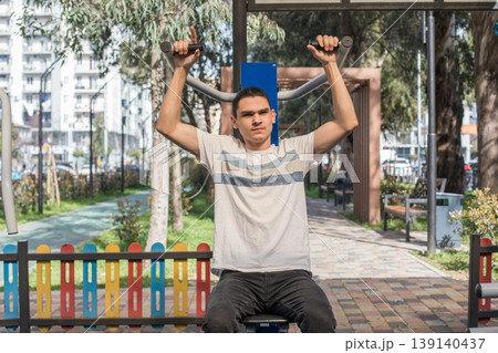 A young man works out in an outdoor gym located in a city park. A young man works out in an outdoor gym located in a city park. 139140437