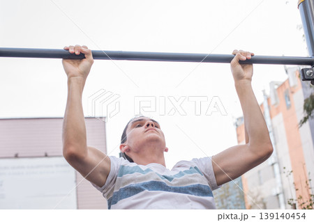A person is performing pull-ups on a metal bar at an outdoor gym. 139140454