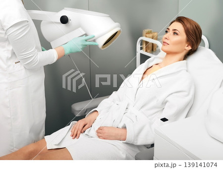 Adult woman during light therapy procedure in a beauty salon with beautician to improve skin appearance and rejuvenation. Phototherapy 139141074