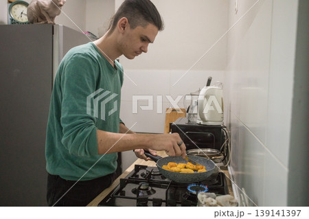 A young man stirs a pot on a stove in a modern kitchen. He is focused on cooking while vegetables A young man stirs a pot on a stove in a modern kitchen. He is focused on cooking while vegetables 139141397