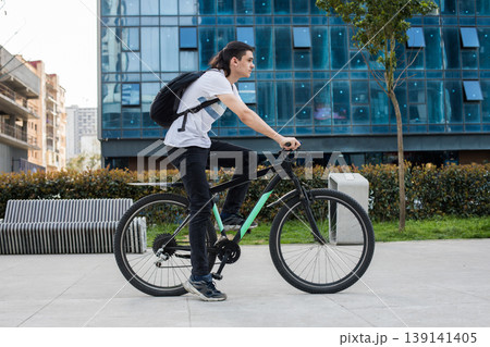 A young man rides a bicycle in a busy city area. Tall buildings surround him as he focuses  139141405