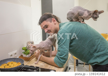 A man stands in a kitchen near a stove while a cat sits on his shoulder.  139141412