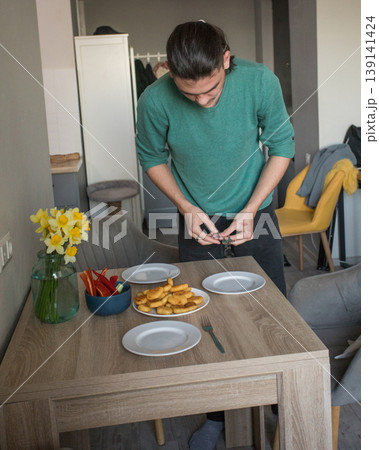 A man is preparing to serve food on the table in a modern room during the afternoon. 139141424
