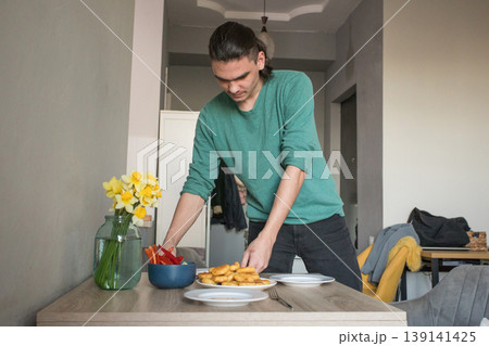 A man is preparing to serve food on the table in a modern room during the afternoon. 139141425