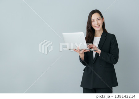 グレーバックのノートパソコンを持つ若いスーツの日本人女性 グレーバックのノートパソコンを持つ若いスーツの日本人女性 139142214