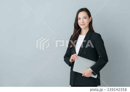 グレーバックのノートパソコンを持つ若いスーツの日本人女性 グレーバックのノートパソコンを持つ若いスーツの日本人女性 139142358