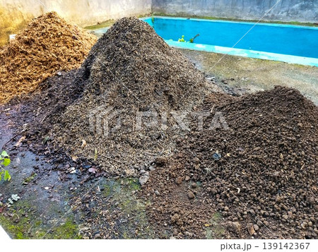 High angle view of three different heaps of organic gardening materials including soil, compost, and rice husks on a wet concrete floor. High angle view of three different heaps of organic gardening materials including soil, compost, and rice husks on a wet concrete floor. 139142367