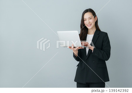 グレーバックのノートパソコンを持つ若いスーツの日本人女性 139142392