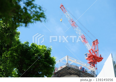 鮮やかな緑越しに見上げる青空と建設クレーンのダイナミックな構図 鮮やかな緑越しに見上げる青空と建設クレーンのダイナミックな構図 139145056