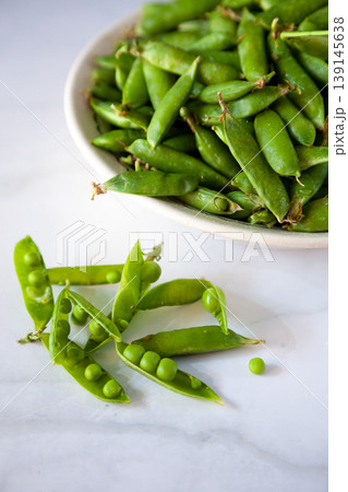 Peas. Green pea pods in a plate on a white table. Harvest. Healthy food close-up. Copy space. 139145638