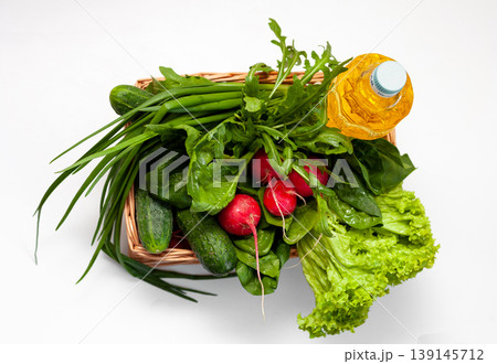 Delivery of products. Box with vegetables and sunflower oil. A set of greens for salad. Chives, lettuce, cucumbers, radishes, spinach, arugula. Isolated on a white background with place for text. 139145712