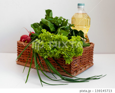 Delivery of products. Box with vegetables and sunflower oil. A set of greens for salad. Chives, lettuce, cucumbers, radishes, spinach, arugula. Isolated on a white background with place for text. 139145713