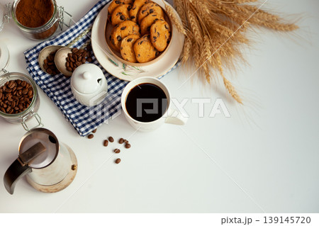White cup of coffee and homemade round cookies with chocolate chips. Breakfast is on the table. Food at home. Still life. Coffee and coffee beans. An invigorating drink. Top view, flat lay. White cup of coffee and homemade round cookies with chocolate chips. Breakfast is on the table. Food at home. Still life. Coffee and coffee beans. An invigorating drink. Top view, flat lay. 139145720