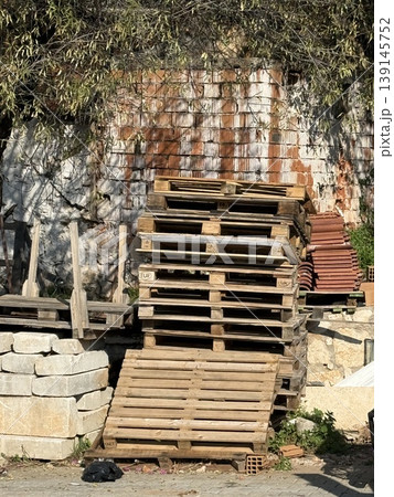 Stack of wooden pallets and bricks near textured wall outdoors, suitable for industrial background 139145752