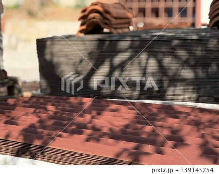 Roof tiles stacked in sunlight with tree shadows, creating an industrial background Roof tiles stacked in sunlight with tree shadows, creating an industrial background 139145754