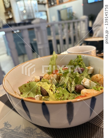 Bowl of fresh salad with lettuce, cherry tomatoes, olives, and feta in cozy dining setting Bowl of fresh salad with lettuce, cherry tomatoes, olives, and feta in cozy dining setting 139145758