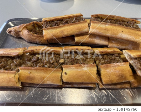Sliced Turkish pide topped with minced meat on metal tray, ideal as food background Sliced Turkish pide topped with minced meat on metal tray, ideal as food background 139145760