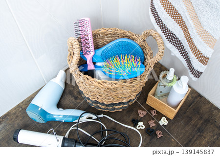 Hair Styling Tools and Accessories in Basket. Bathroom Counter Organization. Hairdryer, towel, curling iron and combs at home. Hairpins and hair care and styling items. Hair Styling Tools and Accessories in Basket. Bathroom Counter Organization. Hairdryer, towel, curling iron and combs at home. Hairpins and hair care and styling items. 139145837