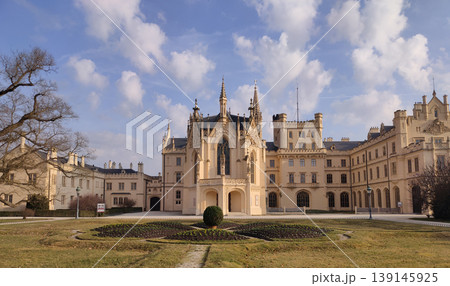 The Lednice castle. Panoramic view of an elaborate castle with an extensive garden and walking paths under a clear blue sky on a sunny afternoon. The Lednice castle. Panoramic view of an elaborate castle with an extensive garden and walking paths under a clear blue sky on a sunny afternoon. 139145925