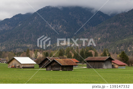 Small wooden houses in green field with mountain forest background Bavaria Germany 139147332