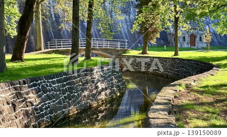 Discover a serene park with a stone wall, river, and bridge Discover a serene park with a stone wall, river, and bridge 139150089