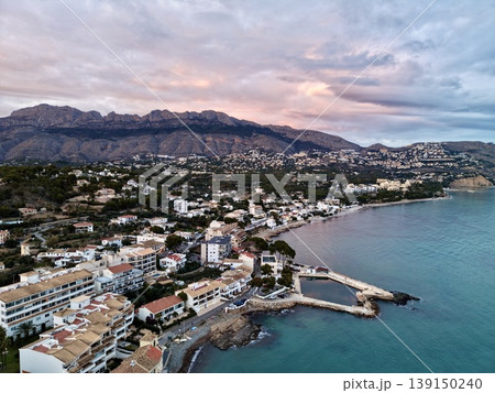 Serene seaside town at sunset, Peaceful shoreline settlement with colorful houses and mountain backdrop 139150240