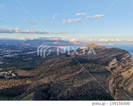 Steep ridges descend into shimmering blue waters, Rustic paths wind across rugged terrain by sea 139150300