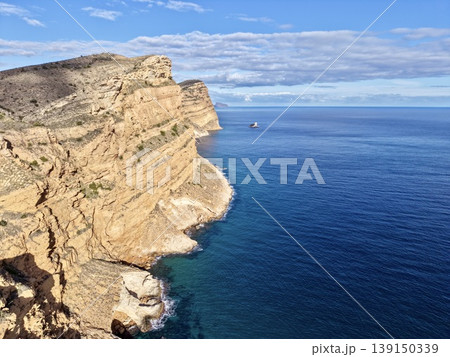 Isolated rocky cove with small harbor beneath towering cliffs and pristine turquoise waters Isolated rocky cove with small harbor beneath towering cliffs and pristine turquoise waters 139150339