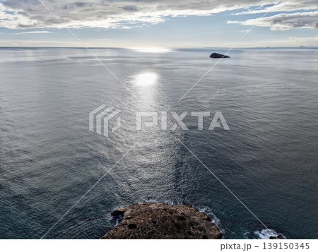 Sunlit path to distant island, Expansive calm waters with gentle cloud cover and scenic coastlines 139150345