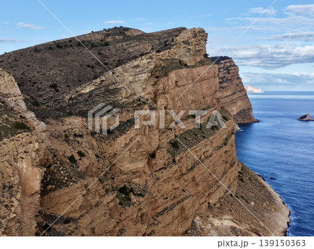 Rock face overview, Close examination of stratified weathered rocks with sparse plant life by sea 139150363
