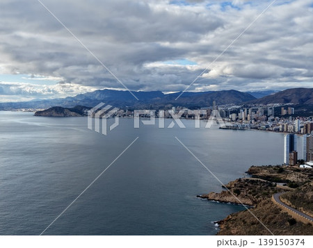 Urban shoreline with mountain backdrop, Highrise buildings along bay with rocky promontory and clouds 139150374