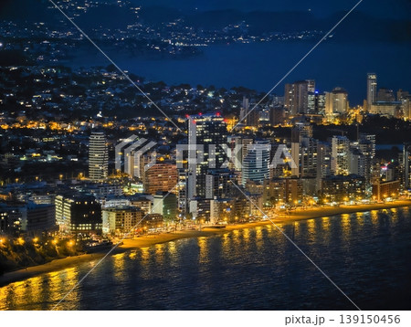 Dynamic coastal urban area illuminated at night with bustling activities and glowing reflections Dynamic coastal urban area illuminated at night with bustling activities and glowing reflections 139150456