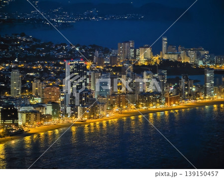 Vivid coastal urban night view. Illuminated skyscrapers and traffic on seaside avenue at night Vivid coastal urban night view. Illuminated skyscrapers and traffic on seaside avenue at night 139150457